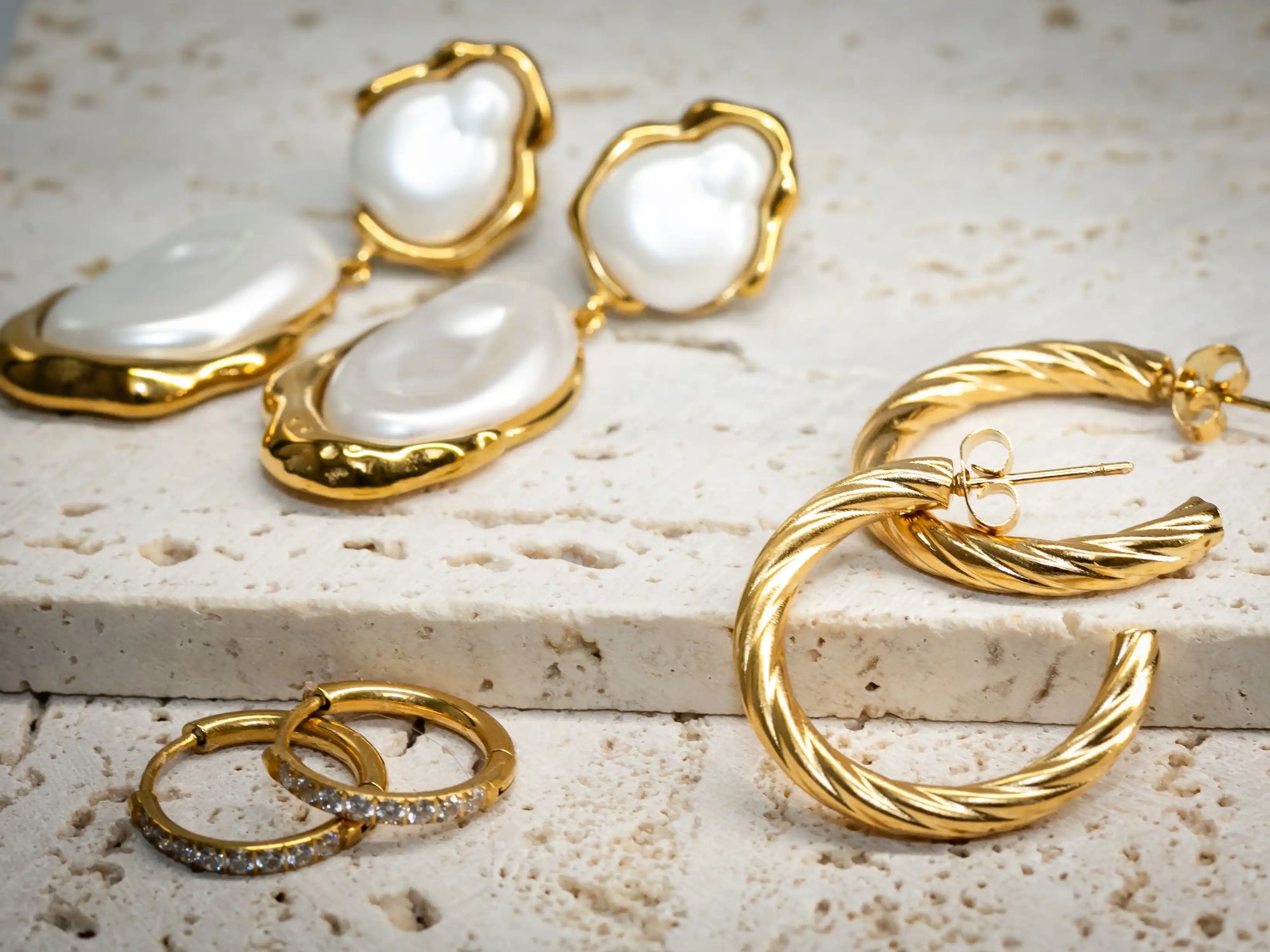 Gold and pearl earrings on a textured surface